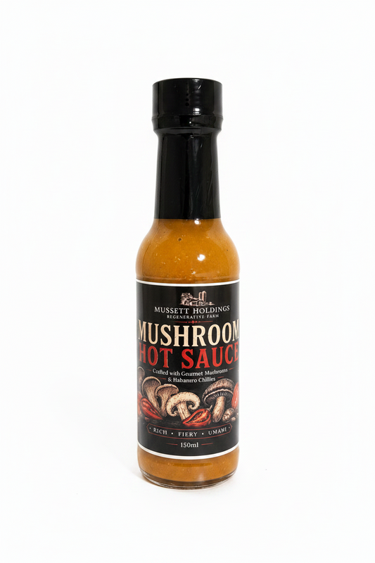 Bottle of Mushroom Hot Sauce surrounded by habanero peppers on a wooden surface